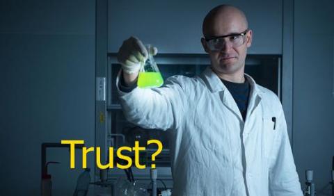 Man in a lab coat holding an erlenmeyer flask with a glowing substance.