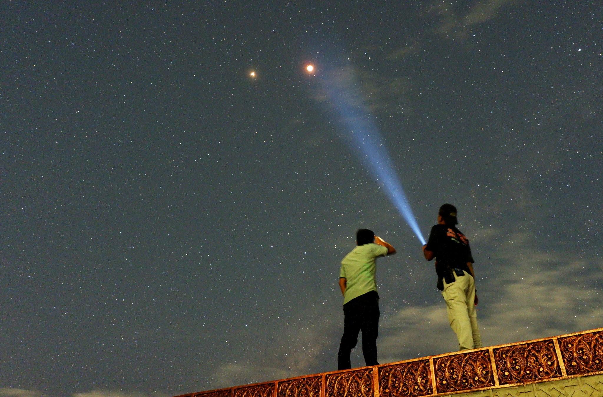 Two men looking up at July 2018's lunar eclipse, where Mars can be seen.